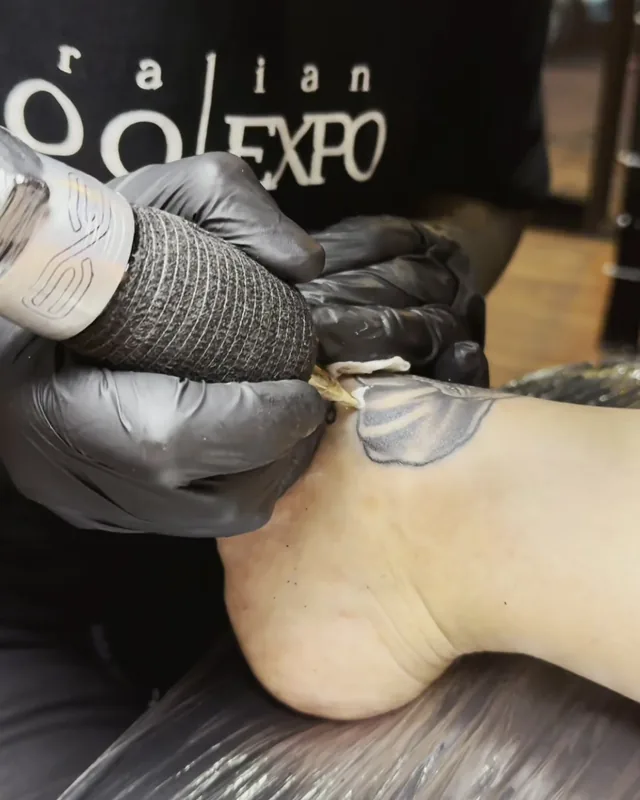Gloved artist using a barrier-wrapped tattoo machine